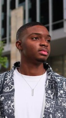 Afro-Amerikalı bir adam uzun ofis binalarının önünde dikiliyor, düşünceli bir ifadeyle kameradan uzağa bakıyor. Sahne kendine güvenen şehir tarzı ve modern şehir yaşamını gösteriyor.