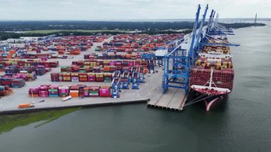 Kalabalık bir sanayi limanına yanaşmış büyük bir konteynır gemisini yakalayan bir İHA atışı. Parlak renkli konteynırlar, vinçler ve deniz altyapısı aktif küresel lojistik gösteriyor.