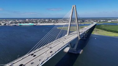 Güney Carolina 'daki şehir kıyılarına uzanan uzun ve modern bir köprünün hava görüntüleri. Sahne, sakin su, uzak binalar ve temiz altyapı ve kıyı manzarasını gösteren temiz bir gökyüzünü içeriyor..