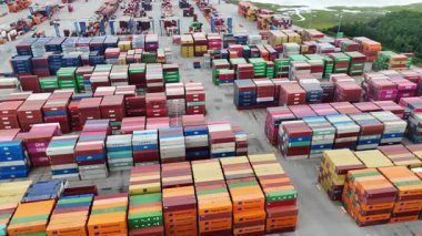 Yoğun bir kargo terminalinde sıkıca istiflenmiş renkli konteynırların yukarıdan aşağıya detaylı bir görüntüsü. Görüntüler küresel ticaret ve lojistik operasyonları vurguluyor