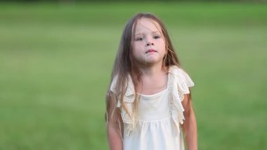 Küçük bir kız yeşil çimenli bir alanda tek başına duruyor, sakin ve düşünceli bir ifadeyle yukarıya bakıyor. Yumuşak doğal ışık ve açık alan huzurlu bir çocukluk anı yaratır..