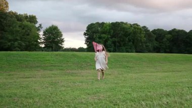 Küçük bir kız küçük bir Amerikan bayrağı taşıyarak geniş yeşil bir tarlada tek başına yürüyor. Barışçıl açık hava sahnesi masumiyeti, özgürlüğü ve sakin bir yaz akşamını vurguluyor..