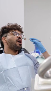 Dikey video. Diş tedavisi sırasında koyu tenli bir Amerikalı 'nın yakın çekimi. Dişçi koltuğundaki adam. Caries 'in modern tedavisi