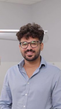 Dişçi ofisinde kameraya bakan siyah saçlı genç bir Amerikalı. Mavi gömlekli, dişçi koltuğunda güzel bir gülümsemesi olan çekici sakallı adam..