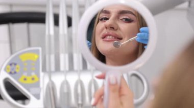 Muayene sırasında dişçi aynasında güzel ve çekici bir kadının yüzü. Bir kadın diş tedavisinin sonucuna bakar..