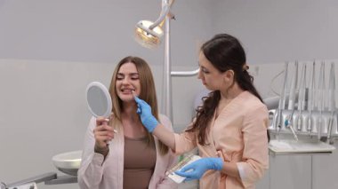 Kadın dişçi hasta için diş rengini ve şeklini seçiyor. Genç hasta dişçi aynasına bakıyor. Modern klinikte dişçi danışmanlığı
