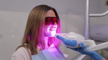 Genç, sarışın bir kadın için diş tedavisi süreci. Doktor ultraviyole lambanın altına polimer yerleştiriyor. Modern diş tedavisi.