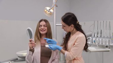 Genç ve çekici bir kadın dişçide muayene oluyor. Doktor diş modelleri arasından dişin rengini ve şeklini seçer..