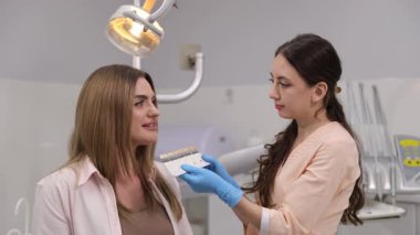 Genç bayan hasta için şekil ve diş rengini seçen pozitif ortodontist. Modern diş kliniğinde genç bir bayan hasta. Sağlıklı bir gülümseme kavramı