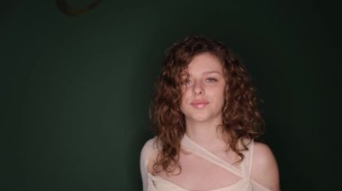 Kıvırcık saçlı bir kadın gözleri kapalı poz verir, yumuşak ve anlamlı bir portre çizer..