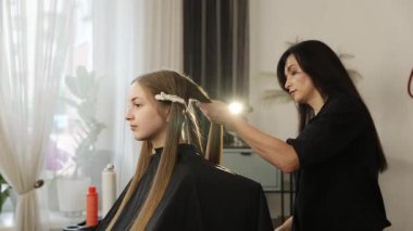 Genç bir bayan müşteri için saç maşası kullanan profesyonel bir kuaför.