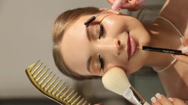 Makyaj sanatçısı, güzellik seansı sırasında rahat bir kadına makyaj malzemesi uyguluyor. Dikey video.