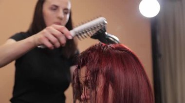 Kuaför kuaför kuaförde saç kurutma makinesi ve fırça kullanarak müşterilerin kuaförde ıslak kızıl saçlarını tarıyor.