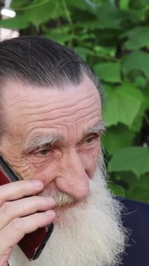 Şehir kaldırımında modern cam binaların yanında duran yaşlı bir adam sakin bir yansıma anında. Dikey video.