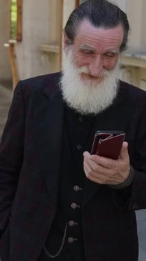 Sakin bir günde kalabalık bir şehir caddesini yüksek binalar ve trafik arasında geçen yaşlı bir adam. Dikey video.