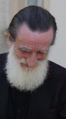 Gri saçlı son sınıf öğrencisi modern binalarla çevrili güneşli bir caddede yürüyor. Dikey video.