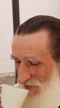 Uzun beyaz sakallı, kırsal bir duvarın ve yeşilliğin yanına bakan son sınıf öğrencisinin yakın çekimi. Dikey video.