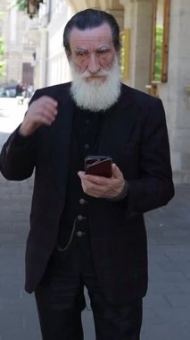 Şehir merkezinde dinlenen kıdemli bir adam sakin bir şehirde insanları ve trafiği izlerken. Dikey video.