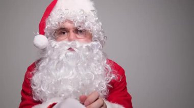 Noel Baba gibi giyinmiş ciddi bir adam gri bir arka plana beyaz eldivenlerini takıyor.