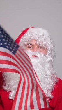 Noel Baba geleneksel kırmızı elbisesiyle Amerikan bayrağını tutuyor ve sallıyor.