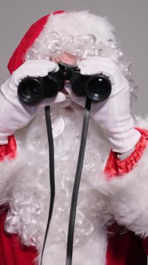 Noel Baba kırmızı giyinmiş, şok olmuş ve şaşırmış bir ifadeyle dürbünle bakıyor.