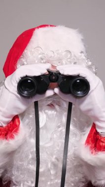 Komik Noel Baba dürbünle bakıyor ve kameraya şaşkın şaşkın bakıyor.