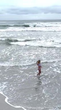 Güzel bir kadın bulutlu bir günde okyanusun sığ sularında yürüyor.