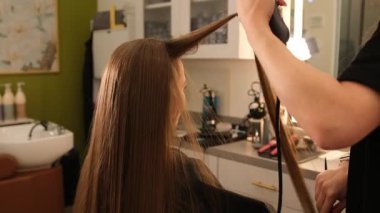 Saç fırçası ve saç kurutma makinesi kullanan kuaför kadın müşterilere uzun kahverengi saç stili veriyor.