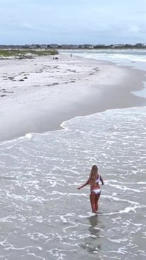 Beyaz bikinili sarışın kadın bulutlu bir günde sığ deniz suyunda oynuyor ve eğleniyor.