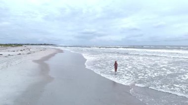 Bulutlu bir günde kumlu bir plajda yürüyen bikinili bir kadın, İHA 'nın hava görüntüsü...