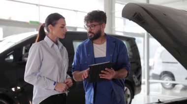 Profesyonel tamirci, araçların sorunlarını tablet kullanan bir kadın müşteriye anlatıyor.