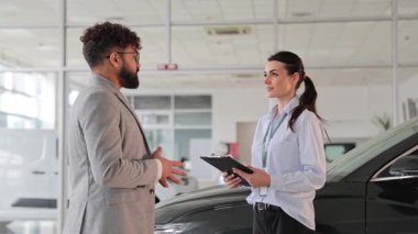 Genç satış müdürü erkek müşteriye danışıyor ve yeni bir araba satarken not alıyor.