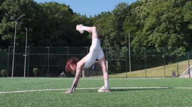 Esnek dövmeli bir kadın amuda kalkıp futbol sahasında antrenman yaparken ayrılıyor.