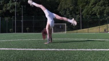 Genç atletik kadın bir spor sahasında arka perende ve akrobatik numaralar yapıyor.