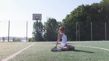Yazın yeşil bir spor sahasında esnek egzersiz yapan dövmeli genç bir atletik kadın.