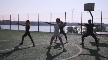 Genç atletik insanlar spor sahasında senkronize esneme ve ısınma egzersizleri yapıyorlar.