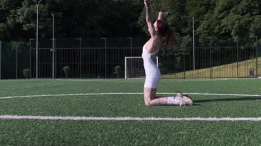 Dövmeli atletik bir kadın açık hava spor sahasında zarif bir yoga akışı uyguluyor.