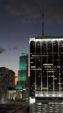 Parlayan Miami gökdeleninin gece hava detayları. Aydınlatılmış pencereleri ve modern şehir tasarımı var. Dikey video.
