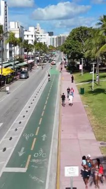 Okyanus Yolu üzerindeki hava manzarası palmiye çizgili sokakları, bisiklet şeritlerini, trafiği ve parlak gün ışığında ikonik sanat deco binalarını yakalıyor. Dikey video.