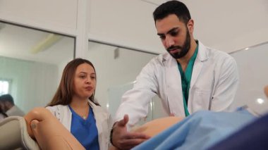 Bir sınıfta doğum simülatörü mankeni kullanarak doğum teknikleri uygulayan genç tıp öğrencileri.