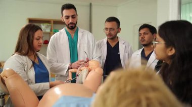 Profesör, çeşitli tıp öğrencilerine doğum simülatörü kullanarak doğum yapmayı öğretiyor.
