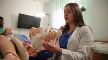 Sınıfta pelvis ve fetal kafa modeli kullanarak kadın doğum eğitimi veren bir eğitmen.