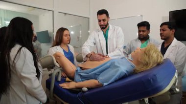 Profesör, doğum simülatörü kullanarak bir grup tıp öğrencisine doğum ve jinekoloji öğretiyor.