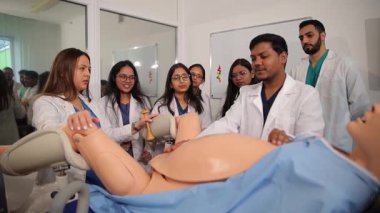 Çeşitli tıp öğrencileri gerçekçi bir doğum simülatörü üzerinde doğum prosedürü uyguluyor.