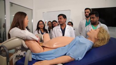 Bir grup tıp öğrencisine doğum simülatörü kullanarak çocuk doğurmayı öğreten kadın doktor.