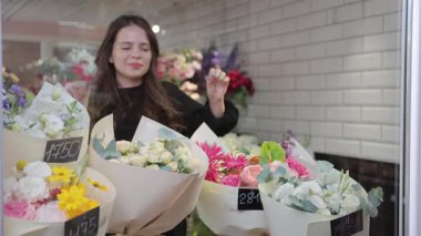 Çiçekçinin vitrininde çiçek buketlerini düzenleyen ve fiyatlandıran genç bir bayan çiçekçi.