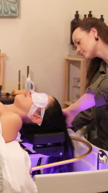 Modern güzellik salonundaki bir kuaförden rahatlatıcı saç yıkama ve kafa masajı alan bir kadın.