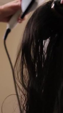 Profesyonel bir kuaför, bir güzellik salonunda saç kurutma makinesi ve yuvarlak bir fırça kullanıyor.