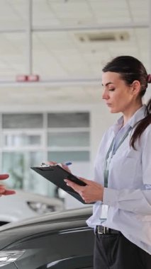 Bir müşteriyle konuşurken panoya yazı yazan dikkatli kadın araba satıcısı.