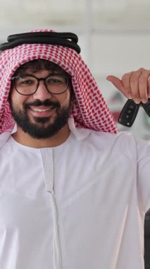 Geleneksel giysiler içinde gülümseyen Arap adam arabanın anahtarlarını tutuyor ve baş parmak işareti yapıyor.
